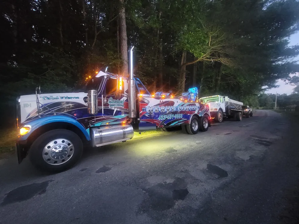 Our heavy wrecker towing a dump truck at dusk with its light bar on