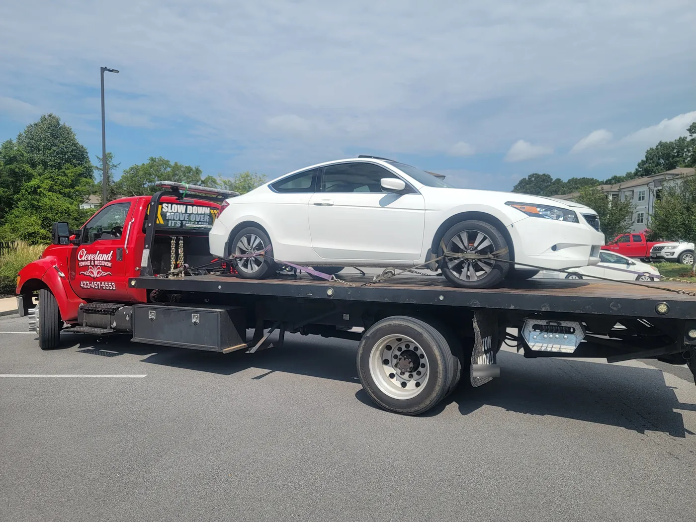 A sedan loaded on our rollback in an apartment parking lot, with a slow down and move over sign on the boom